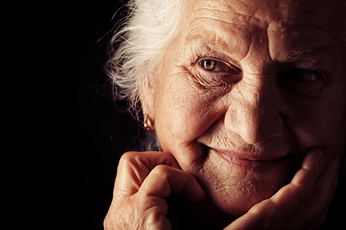Close of up senior woman smiling with her hands on her cheeks and chin and a black background